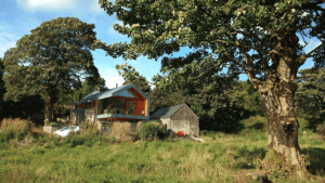 The open glass box of the main living area in the Copper Barn is striking, yet still sits sympathetically with the old undeveloped stone barn next door and the lush green trees and meadow around it
